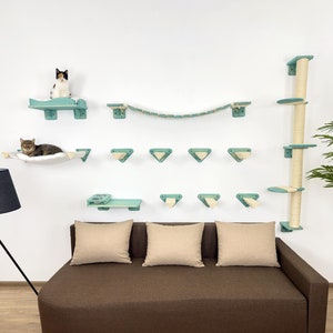 May include: A teal blue cat tree with multiple platforms, a hammock, and a bridge. The cat tree is mounted on a white wall. A brown couch with three beige cushions is in the foreground.