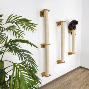 May include: Three wall-mounted cat scratching posts with sisal rope covered posts. The posts are different heights and are mounted on a white wall. A gray cat is sitting on the top of the shortest post.