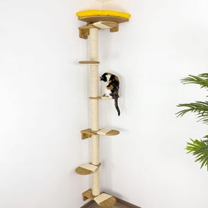 May include: A corner cat tree with a yellow cushion on top, a sisal-covered scratching post, and multiple platforms. A calico cat is sitting on one of the platforms.