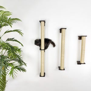 May include: Three wall-mounted cat scratching posts with sisal rope covered posts. The posts are different heights and are mounted on a white wall. A black cat is climbing one of the posts.