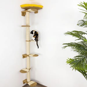 May include: A tall, wooden cat tree with a sisal-covered scratching post and multiple platforms. The cat tree is mounted in a corner and has a yellow platform at the top. A cat is sitting on one of the platforms.