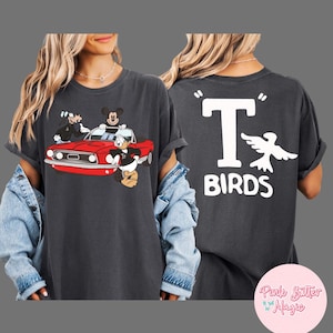 May include: Dark gray t-shirt featuring a cartoon image of Mickey Mouse, Donald Duck, and Goofy in a red car. The back of the shirt displays the text "T BIRDS" with a white bird graphic.