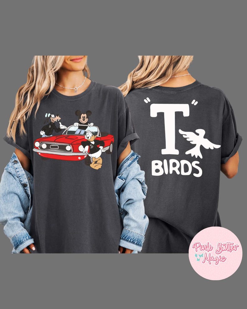 May include: Dark gray t-shirt featuring a cartoon image of Mickey Mouse, Donald Duck, and Goofy in a red car. The back of the shirt displays the text "T BIRDS" with a white bird graphic.