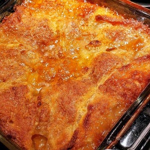 May include: A golden brown baked dessert with a crispy top and a gooey, caramelized sauce. The dessert is in a clear glass baking dish.