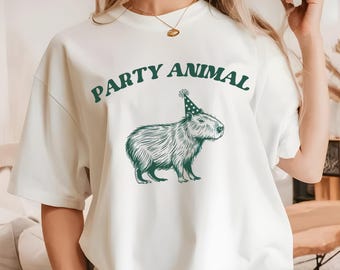May include: White t-shirt with a green graphic of a capybara wearing a party hat. The text "PARTY ANIMAL" is printed above the capybara.