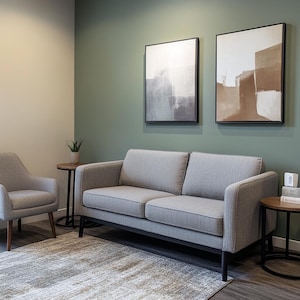 Könnte beinhalten: Ein modernes Wohnzimmer-Setup mit einem grauen Zweisitzer-Sofa und einem passenden Sessel. Zwei abstrakte Gemälde hängen an einer grünen Wand. Ein runder Beistelltisch mit einer kleinen Pflanze und ein Teppich vervollständigen die Einrichtung.