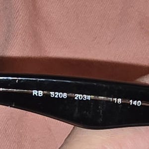 Pu&ograve; includere: Primo piano dell'asta di occhiali da sole neri. Il testo "RB 5208 2034 18 140" &egrave; stampato in bianco all'interno dell'asta. L'asta &egrave; tenuta da una persona.