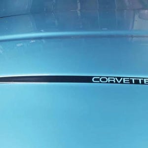 May include: A light blue car bonnet featuring a black accent stripe and the word "CORVETTE" in white lettering. The bonnet has a glossy finish and is slightly curved.