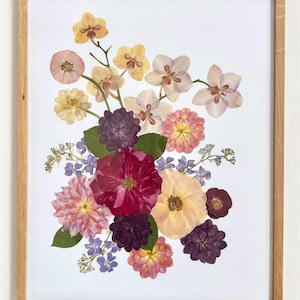 May include: A framed floral art print featuring a vibrant arrangement of pressed flowers in shades of yellow, pink, purple, and red. The flowers are arranged on a white background and framed in a natural wood frame.