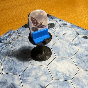 May include: A black and blue game piece with a circular base and a blue stand. The piece features a printed image of a bird with purple accents against a cloudy background.