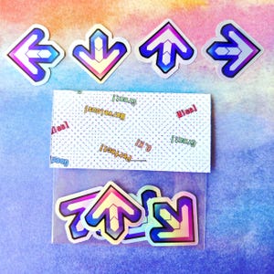 May include: A set of colorful arrow stickers with a holographic effect, in blue, pink, and yellow. The stickers are arranged with a small card that has the words "Perfect!", "O.K!", "Great!", "Marvelous!", and "Miss!" printed on it.