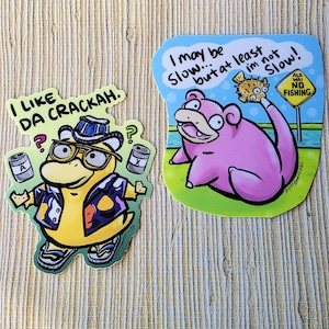 May include: Two colorful stickers featuring cartoon characters. One shows a yellow character in a hat and glasses with the text "I LIKE DA CRACKAH." The other depicts a pink character with the text "I may be slow... but at least I'm not slow!"