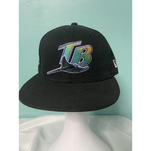Puede incluir: Gorra de béisbol negra con el logotipo de los Tampa Bay Rays. El logotipo incluye las letras "TB" en un degradado verde, azul y amarillo, con una raya estilizada. La gorra tiene una visera curva y un logotipo de New Era en el lateral.