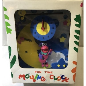 May include: A boxed children's clock with a blue clock face, yellow hands, and a cartoon dog playing a guitar. The clock has a yellow moon, blue stars, and the words "FUN TIME MOVING CLOCK" on the box.