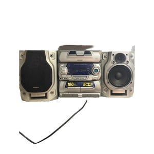 以下が含まれることがあります： 2つのスピーカーと中央ユニットを備えたシルバーのステレオシステム。中央ユニットには、CDプレーヤー、ラジオ、カセットプレーヤーがあります。スピーカーは長方形で、黒いスピーカーカバーが付いています。電源コードが見えます。