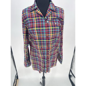 May include: A long-sleeved plaid shirt in a vibrant mix of colors, including red, yellow, blue, and green. The shirt features a classic collar, button-down front, and a small pocket detail. The plaid pattern is evenly spaced.