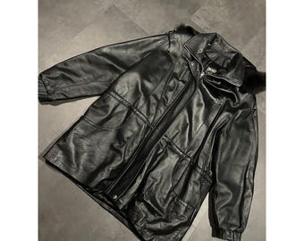 Könnte beinhalten: Schwarze Lederjacke mit Pelzkragen. Die Jacke hat einen Reißverschluss, mehrere Taschen und den Markennamen "IMAGE" auf dem Etikett. Die Jacke liegt flach auf einer grauen Oberfläche.