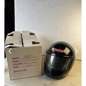 May include: A glossy black full-face motorcycle helmet with a tinted visor and the word Vector in red lettering on the front. Next to it is a cardboard box with printed text including PART#, DESC. VS 200 SNO MAX, COLOR BLACK, SIZE Med, and MADE IN USA.