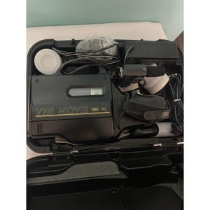 May include: Black VHS Movie HQ camcorder kit in a black carrying case. The kit includes a camcorder, power adapter, cables, and other accessories. The words "VHS MOVIE" and "VHS HQ" are printed on the camcorder.