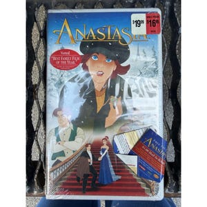 Op de afbeelding: Een verzegelde VHS-band van de animatiefilm Anastasia met een centraal personage in een zwarte hoed en jas, een mannelijk personage in een groen vest en een koppel op een rode trap. Een rode sticker toont de tekst Voted Best Family Film of the Year.