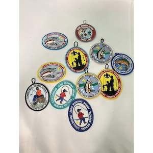 Puede incluir: Una colección de parches bordados con diseños de pesca. Los parches presentan imágenes de peces, pescadores y textos como "Annual Fishing Derby" y "Connecticut Yankee Council". Los colores incluyen azul, rojo, amarillo y verde.