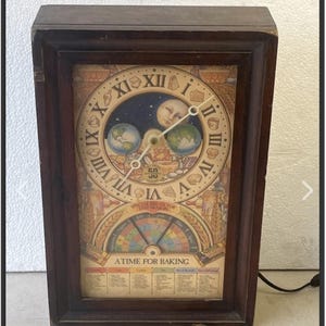 May include: A rectangular wooden wall clock featuring a central circular face with Roman numerals, a moon illustration, and two globes. Below the clock face is a colorful seasonal calendar dial labeled A TIME FOR BAKING and Nestle branding.