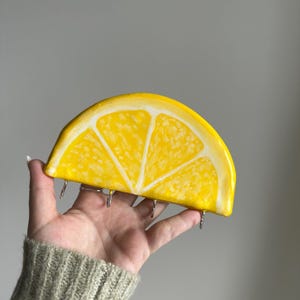 May include: A yellow ceramic lemon slice key holder with five metal hooks. The lemon slice is painted with white lines to resemble the inside of a lemon.