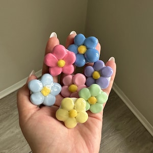 May include: A set of six pastel-colored ceramic flower-shaped buttons. The flowers are in shades of pink, blue, yellow, and green.
