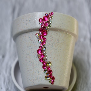 May include: White ceramic flower pot with a decorative design of pink and iridescent rhinestones.