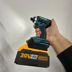 Könnte beinhalten: Ein kabelloser Makita Schlagschrauber in Türkis und Schwarz mit integrierter LED-Leuchte. Er wird von einem 20V MAX 4.0Ah Akku in Schwarz und Orange angetrieben. Auf dem Akku steht das Wort SHARE.