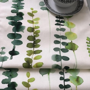 May include: A white table runner with a green watercolour leaf pattern. The runner is folded in thirds and has a white background with green leaves.