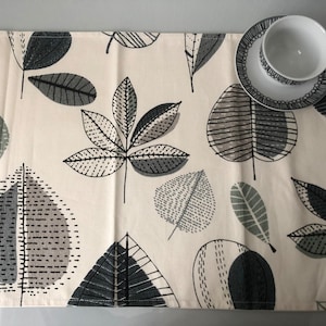 May include: A white table runner with a black and grey leaf pattern. The runner is made of fabric and has a subtle texture.