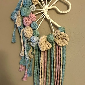 May include: A macrame unicorn wall hanging with a white base and pastel pink, blue, and beige yarn. The unicorn is made of yarn and has a mane and tail with tassels.