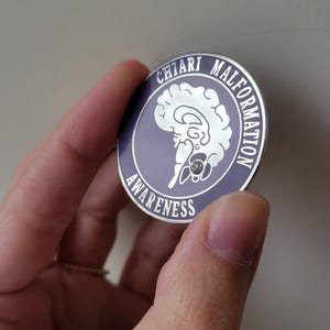 May include: A purple and silver pin with a brain outline and the text "Chiari Malformation Awareness".