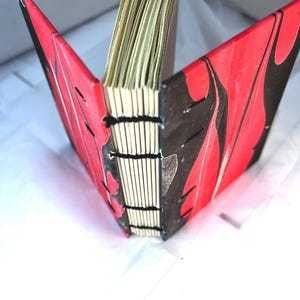 May include: A small, red and black marbled notebook with a bound spine. The notebook is closed and standing upright.