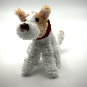May include: A handmade terrier dog figurine with a white body, tan and brown head, and a red collar. The dog is made of a soft, textured material and stands on four legs, with its tail slightly raised.