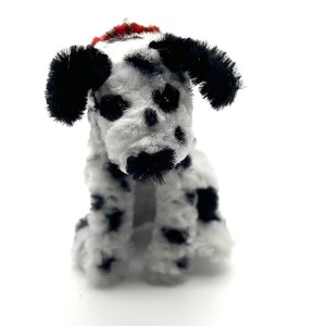 May include: A handcrafted Dalmatian dog figure made from white and black pipe cleaners. The dog features black spots, ears, and nose, with a red accent on its head. The figure is in a seated position, highlighting its detailed construction.