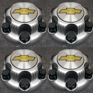 May include: Four silver wheel center caps with a yellow and black Chevrolet logo. Each cap has a circular design with black lug nuts around the perimeter. The caps are arranged in a square formation.