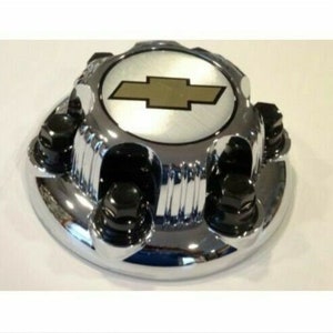 May include: A circular chrome wheel center cap featuring a central silver emblem with a black Chevrolet bowtie logo. The exterior rim includes four integrated black lug nut covers arranged symmetrically around the polished metallic surface.
