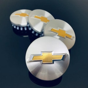 May include: Four silver car hubcaps with a gold Chevrolet logo. The hubcaps are arranged in a semi-circle.