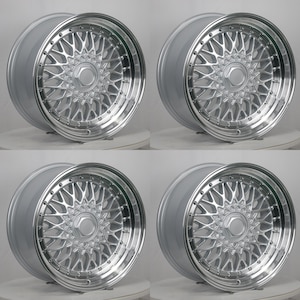 May include: A set of four silver-colored automotive wheels featuring a multi-spoke mesh design. Each wheel has a polished outer rim, a central hexagonal hub cap, and a series of small decorative bolts encircling the inner edge of the rim.