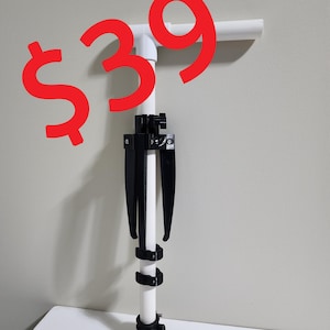 Puede incluir: Un tubo de PVC blanco con un trípode ajustable negro conectado. El tubo tiene un conector en T en la parte superior. El precio es de 39 €.