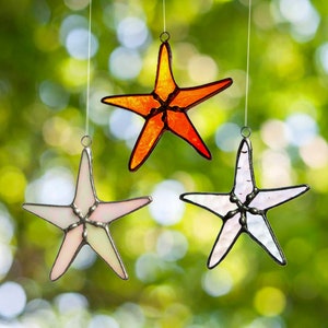 May include: Three stained glass starfish ornaments hanging from strings. One is orange, and two are white with a pearlescent finish.