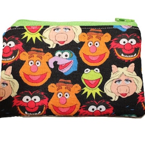May include: A black zippered pouch with a colorful pattern of Muppet characters, including Kermit the Frog, Miss Piggy, and Animal.
