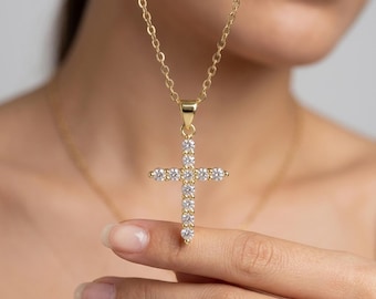 May include: A gold-toned necklace featuring a cross pendant set with eleven clear, round-cut stones. The pendant hangs from a delicate gold-toned chain, with the cross design composed of a vertical row of seven stones and a horizontal row of four.
