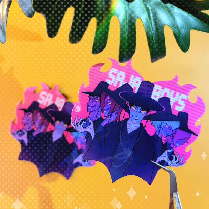 May include: Holographic stickers featuring a group of stylized characters with blue skin, wearing black hats and robes. The stickers have a pink and purple flame-like border with the text "SA IA BOYS". The background is yellow.