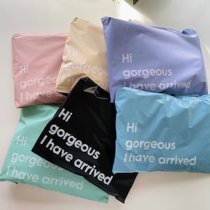 Puede incluir: Seis sobres de envío de polietileno de colores con el texto "Hi gorgeous I have arrived" impreso en ellos. Los sobres son de varios colores, incluyendo rosa, beige, azul claro, azul oscuro, negro y verde claro.