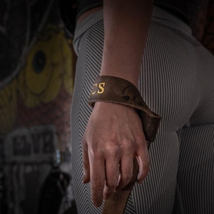 Puede incluir: Correa de muñeca de cuero marrón con letras doradas que dicen "CS".