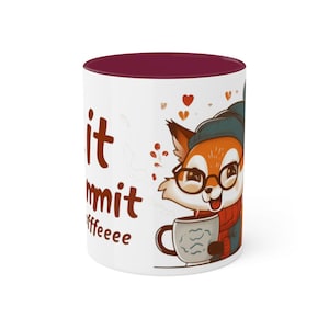 May include: White ceramic mug with a burgundy rim. The mug features a cartoon fox wearing glasses and a scarf, holding a cup of coffee. The text "Git it Commit Offeeee" is printed on the mug.