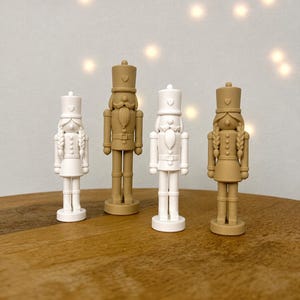 Könnte beinhalten: Vier stehende Nussknacker-Figuren in einer Reihe. Zwei sind einfarbig weiß und zwei sind einfarbig beige. Jede Figur trägt einen hohen Hut mit einem kleinen Herzdetail. Zwei Figuren haben geflochtenes Haar, die anderen zwei einen Schnurrbart.